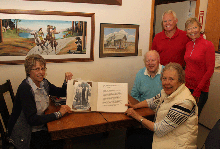 Janet Carlson (foreground right), shows Renee Geving the book she wote about Doc’s Lodge as husband Roger Carlson, daughter Kristin Vlasak and son-in-law Gordon Vlasak look on. Carlson recently donated the book to the Cass County Historical Society.